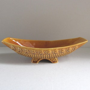 May include: A brown ceramic planter with a decorative design of stylised flowers around the rim. The planter has three legs and is shaped like a boat.