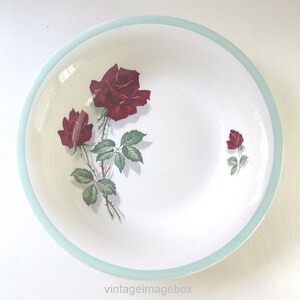 May include: White ceramic bowl with a pale blue rim and a floral rose design. The bowl features three red roses with green leaves. A vintage serving dish.