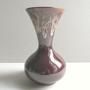 May include: A glossy, dark burgundy ceramic vase with a bulbous base and flared top. The rim has a textured, off-white and brown pattern. The vase is approximately 18 cm tall, suitable for displaying flowers or as a decorative piece.