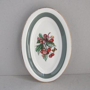 May include: Oval serving platter with a white centre, a green border, and a gold rim. The centre features a cluster of red cherries with green leaves and a small butterfly. A decorative piece for serving.