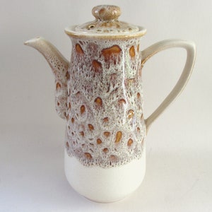 May include: A ceramic coffee pot with a lid and handle. The pot has a white base and a textured upper section with brown and cream patterns. The spout and handle are cream-coloured.
