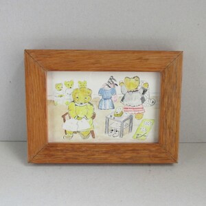 May include: A framed watercolor painting featuring anthropomorphic teddy bears in a domestic scene. The bears are depicted in various outfits, with a yellow bear seated and others standing near furniture. The frame is made of light brown wood.