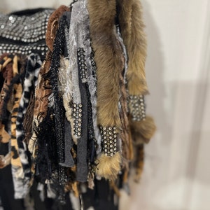 Puede incluir: Una bolsa negra con una variedad de flecos de tela de colores, incluyendo piel sint&eacute;tica, estampado de leopardo y tela gris. La bolsa est&aacute; decorada con pedrer&iacute;a.