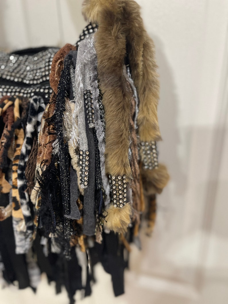 Puede incluir: Una bolsa negra con una variedad de flecos de tela de colores, incluyendo piel sint&eacute;tica, estampado de leopardo y tela gris. La bolsa est&aacute; decorada con pedrer&iacute;a.