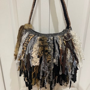 Puede incluir: Un bolso tote negro y marr&oacute;n con flecos y ribete de strass. El bolso est&aacute; hecho de varias telas, incluyendo piel sint&eacute;tica, y tiene una correa larga.