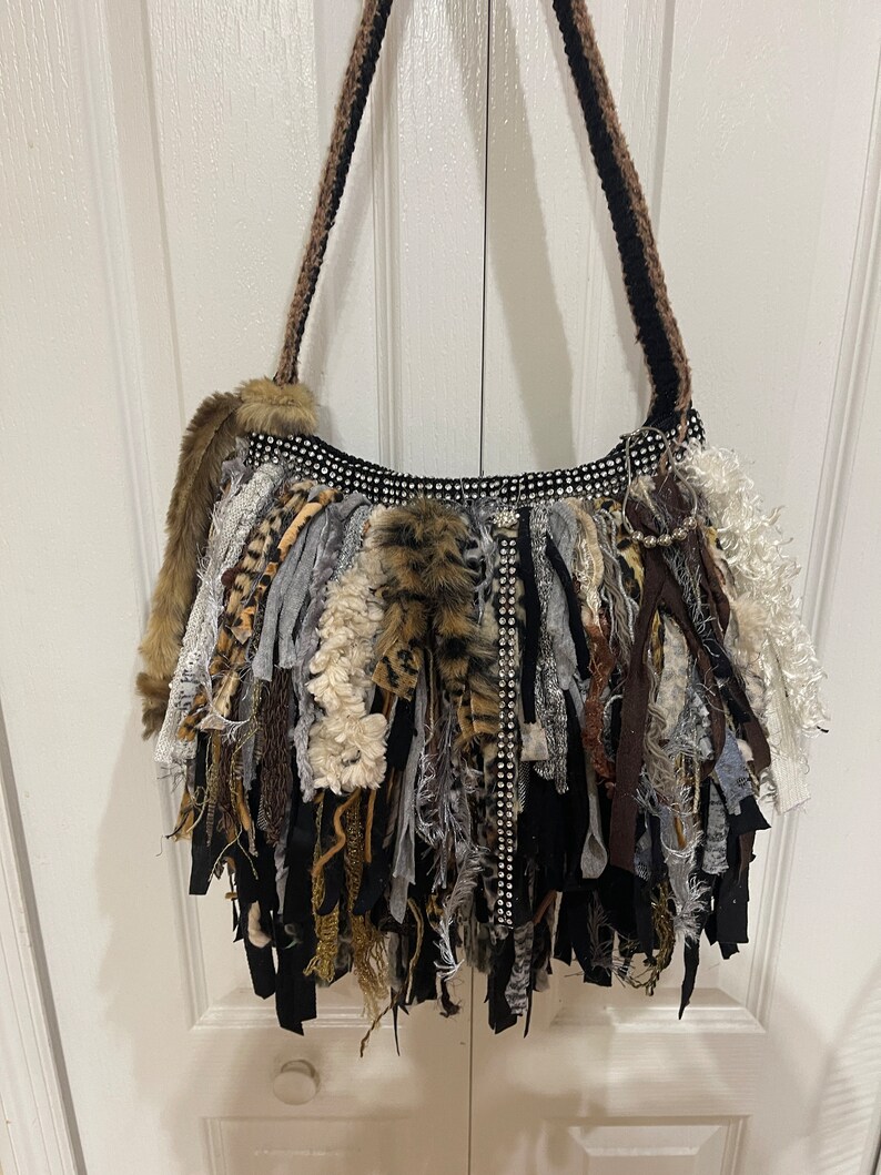 Puede incluir: Un bolso tote negro y marr&oacute;n con flecos y ribete de strass. El bolso est&aacute; hecho de varias telas, incluyendo piel sint&eacute;tica, y tiene una correa larga.