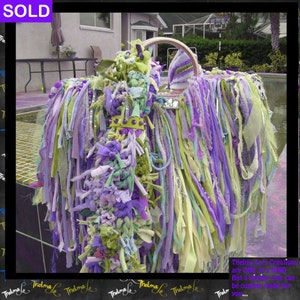 May include: A purple, green, and white fabric handbag with a silver handle and a beaded embellishment. The bag is made of strips of fabric that are tied together. The text "Thelma Le's Creations are One of a Kind But a similar one can be custom made for you..." is visible at the bottom of the image.