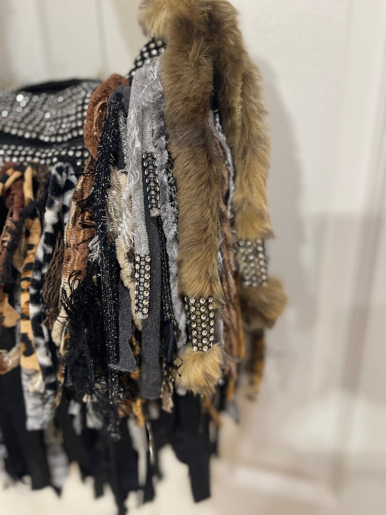 Puede incluir: Una bolsa negra con una variedad de flecos de tela de colores, incluyendo piel sint&eacute;tica, estampado de leopardo y tela gris. La bolsa est&aacute; decorada con pedrer&iacute;a.