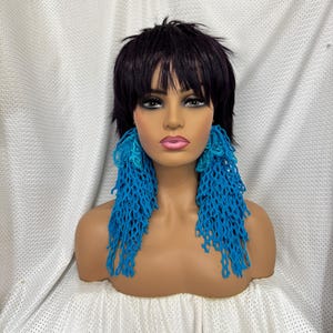 May include: A mannequin with short black hair wearing long, blue, crocheted earrings.
