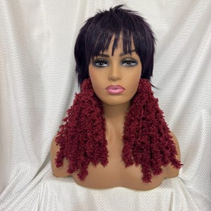 May include: A pair of long, burgundy, fuzzy earrings. The earrings are made of yarn and have a shaggy, textured look.