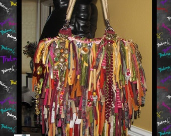 May include: A colourful, bohemian-style handbag with a fringe design. The bag is made of various fabrics and textures, including leather, suede, and beads. It features a variety of embellishments, such as tassels, charms, and beads.