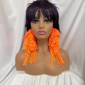 May include: A pair of bright orange statement earrings with a net-like design. The earrings are long and dangle, with a layered effect.