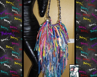 May include: A colourful, multi-layered, fringed handbag with a brown beaded strap. The bag is made from a variety of fabrics, including denim, cotton, and silk. The bag is sold.