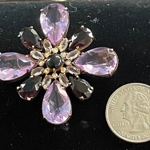 May include: A large, pink and black flower-shaped brooch with a central black stone surrounded by smaller clear stones. The brooch is about the size of a quarter.