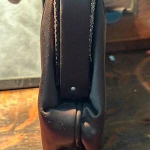 May include: A dark brown satin clutch bag with a zip closure and a silver chain strap.