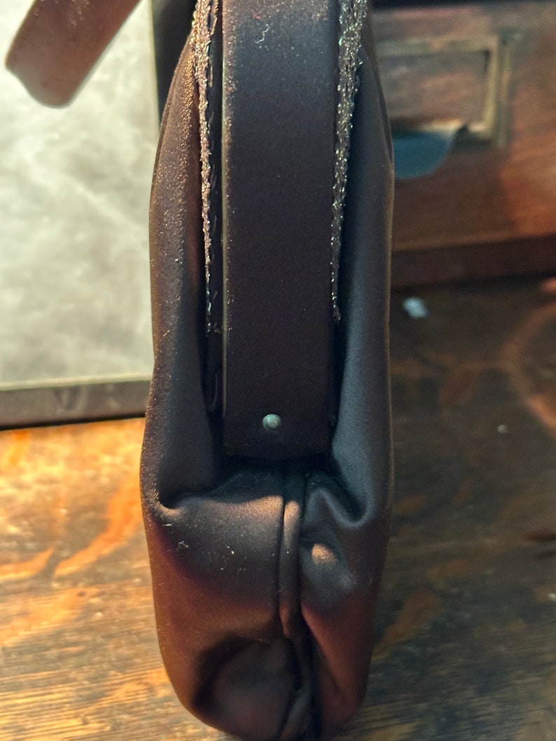 May include: A dark brown satin clutch bag with a zip closure and a silver chain strap.