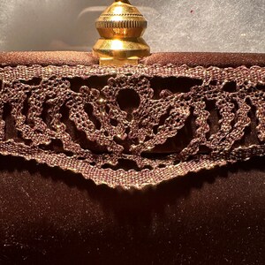 May include: A brown velvet clutch with a gold metal clasp and a lace trim.