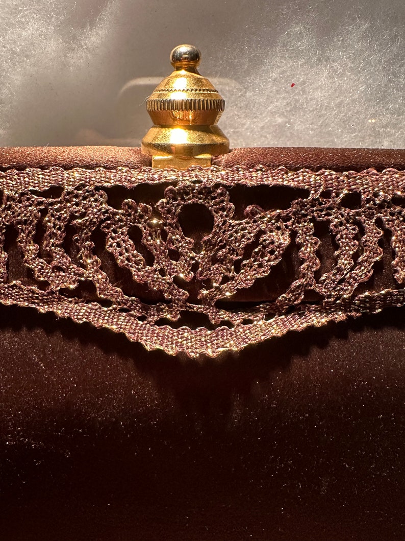 May include: A brown velvet clutch with a gold metal clasp and a lace trim.