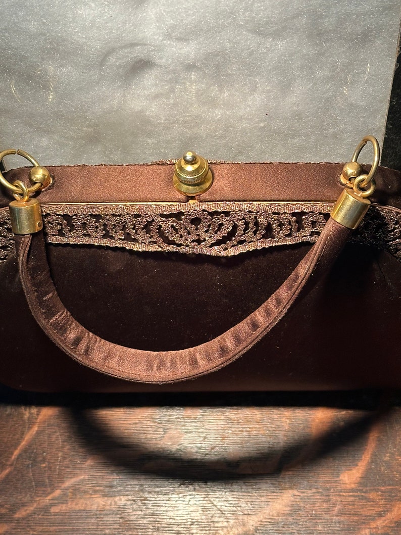 May include: A brown velvet evening bag with a gold clasp and a lace trim. The bag has a single strap and a gold top handle.