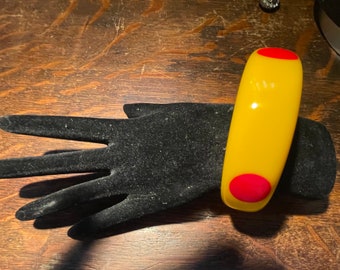 May include: A yellow plastic bangle bracelet with two red circles on the front.