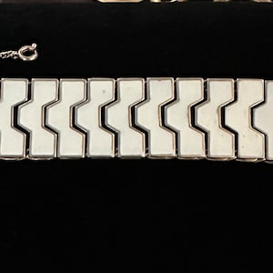 May include: A silver and white bracelet with a geometric design. The bracelet is made of interlocking links that form a zig-zag pattern.