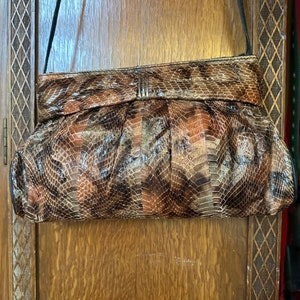 May include: A brown snakeskin clutch purse with a silver clasp and a black shoulder strap.