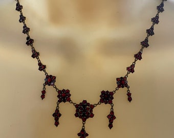 May include: A vintage garnet necklace with a delicate design. The necklace features a central cluster of garnets with smaller clusters cascading down on either side. The garnets are a deep red color and are set in a silver-toned metal.