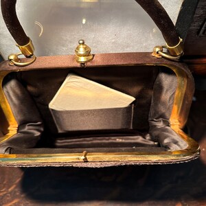 May include: A brown velvet handbag with a gold clasp and a gold handle. The bag is open and the inside is lined with a brown fabric.