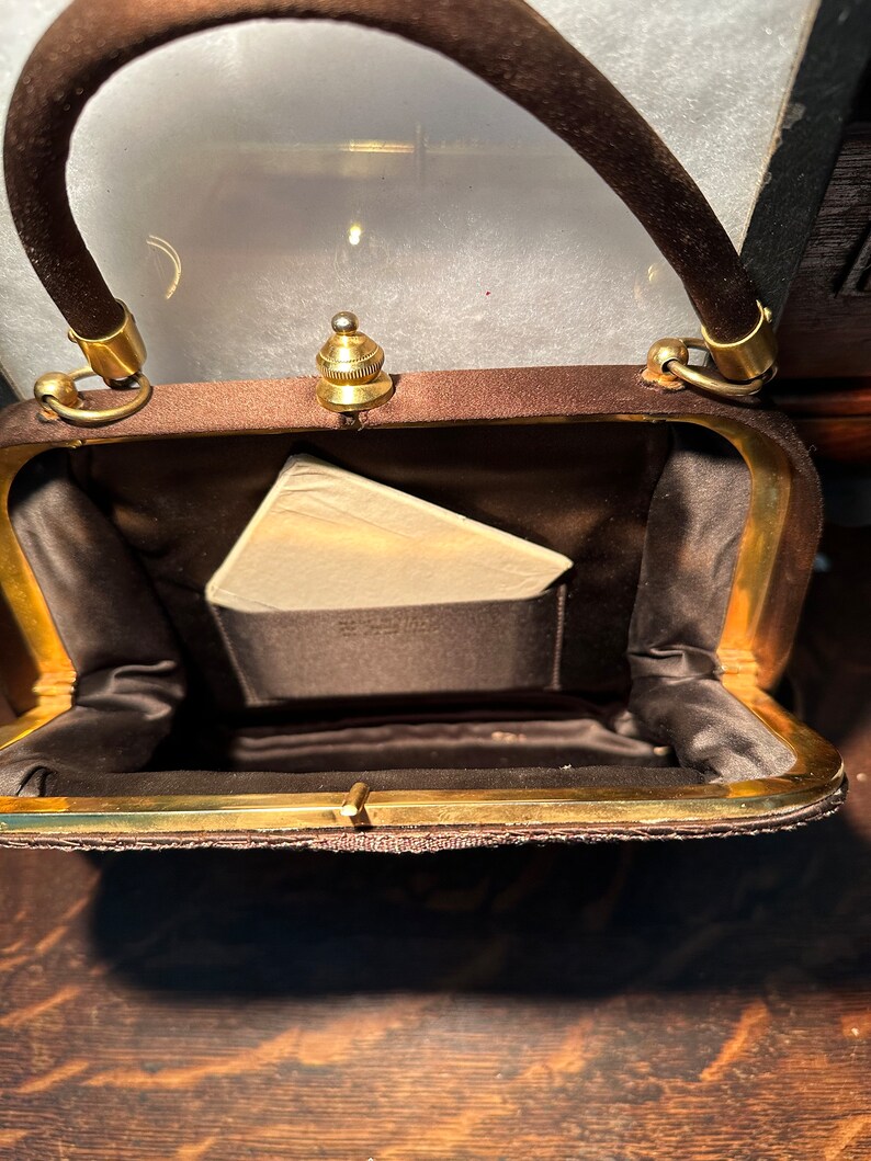May include: A brown velvet handbag with a gold clasp and a gold handle. The bag is open and the inside is lined with a brown fabric.