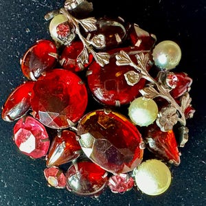 May include: A vintage brooch featuring a cluster of red and clear glass stones, set in silver tone metal with a delicate floral design.
