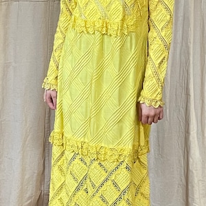 May include: A yellow maxi dress with a lace overlay and a diamond pattern. The dress has a high neckline and long sleeves.
