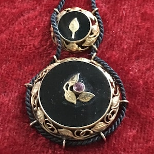 May include: A black onyx pendant necklace with gold filigree and a small pink stone. The necklace is on a black cord.