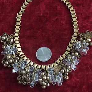 May include: A gold chain necklace with clear crystal and gold bead accents. The necklace has a dangling design with multiple strands of beads and crystals.