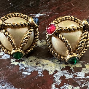 May include: A pair of gold tone earrings with a faux pearl center and colorful stones. The stones are red, green, and blue.