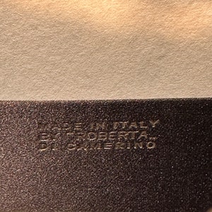 May include: Close-up of a black leather tag with white text that reads "Made in Italy Roberta&trade;  CATERINO".