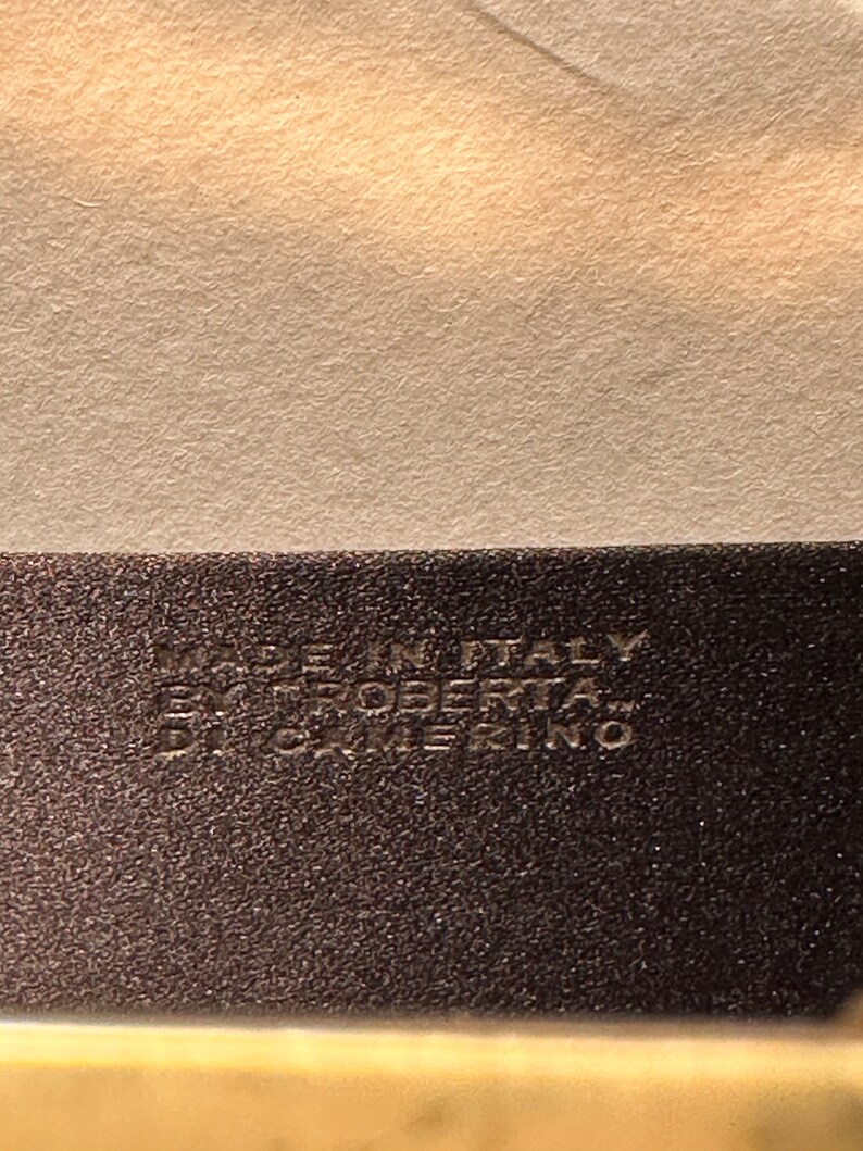 May include: Close-up of a black leather tag with white text that reads "Made in Italy Roberta&trade;  CATERINO".