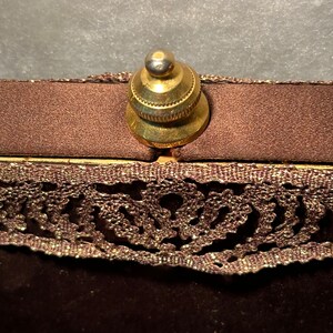 May include: A brown velvet bag with a gold metal clasp and a lace trim. The bag has a decorative design on the lace.