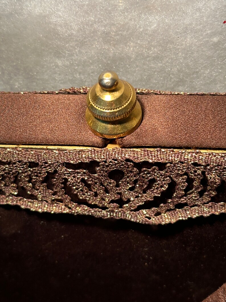 May include: A brown velvet bag with a gold metal clasp and a lace trim. The bag has a decorative design on the lace.