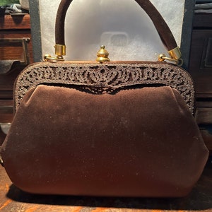 May include: A brown velvet handbag with a gold metal clasp and a decorative lace trim. The handbag has a brown velvet handle.