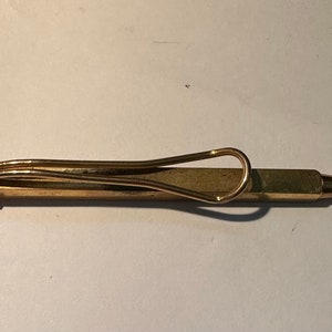 May include: A gold-toned metal pen with a retractable tip and a decorative clip. The pen is lying on a white surface.