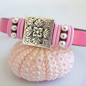 May include: A pink leather bracelet with a silver floral charm and silver beads.