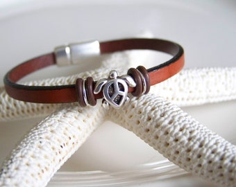 May include: A brown leather bracelet with a silver turtle charm featuring a peace sign. The bracelet has a magnetic clasp.