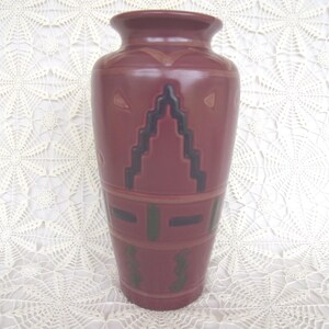 May include: A maroon ceramic vase with a wide base and a narrower neck. The vase features geometric designs in black, green, and tan. The vase is approximately 12 inches tall.