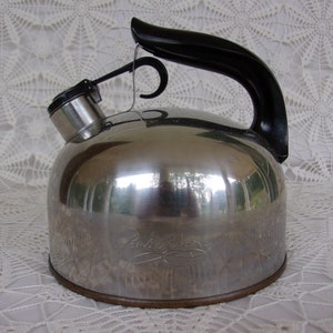 May include: A stainless steel Paul Revere tea kettle with a black handle and spout. The kettle has a rounded body and a shiny, reflective surface. The brand name is etched on the side.