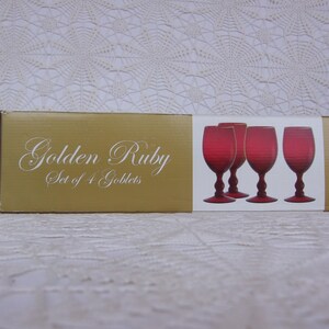 May include: A box of Golden Ruby goblets. The box is gold with white script. Four red wine glasses are visible on the box. The glasses have a textured design and a red base.
