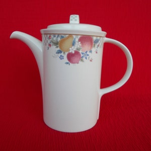 May include: White ceramic coffee pot with a lid and handle. The pot features a fruit and floral design around the top, including apples, pears, and flowers. The spout is long and curved. The background is a solid red.