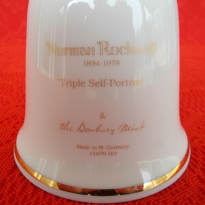 May include: White porcelain bell with a gold trim. The bell features a gold inscription that reads "Norman Rockwell 1894-1978 Triple Self-Portrait" and "The Danbury Mint Made in W. Germany &copy;1979 SEP".