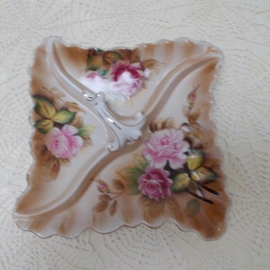 May include: A white porcelain serving dish with three sections. The dish is decorated with pink and yellow roses and green leaves. The dish has a scalloped edge.