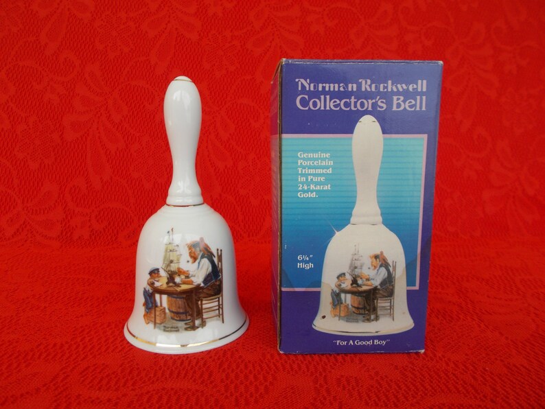May include: White porcelain bell with a gold trim, featuring a Norman Rockwell illustration of a man and a boy building a ship. The bell is 6 1/2 inches high and comes in a blue box with the text "Norman Rockwell Collector's Bell" and "For A Good Boy".