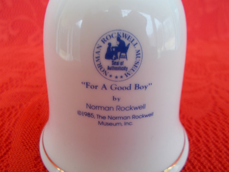May include: White ceramic bell with a blue and white Norman Rockwell Museum seal and the text "For A Good Boy" by Norman Rockwell &copy;1985, The Norman Rockwell Museum, Inc.